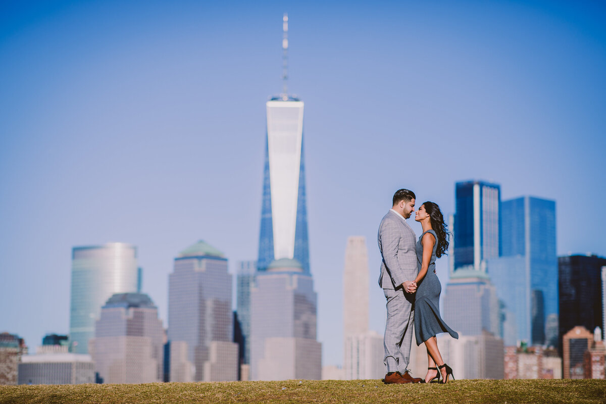 An engaged couple standing at the top of a hill sharing a moment together at liberty state park in nj with the nyc skyline in view