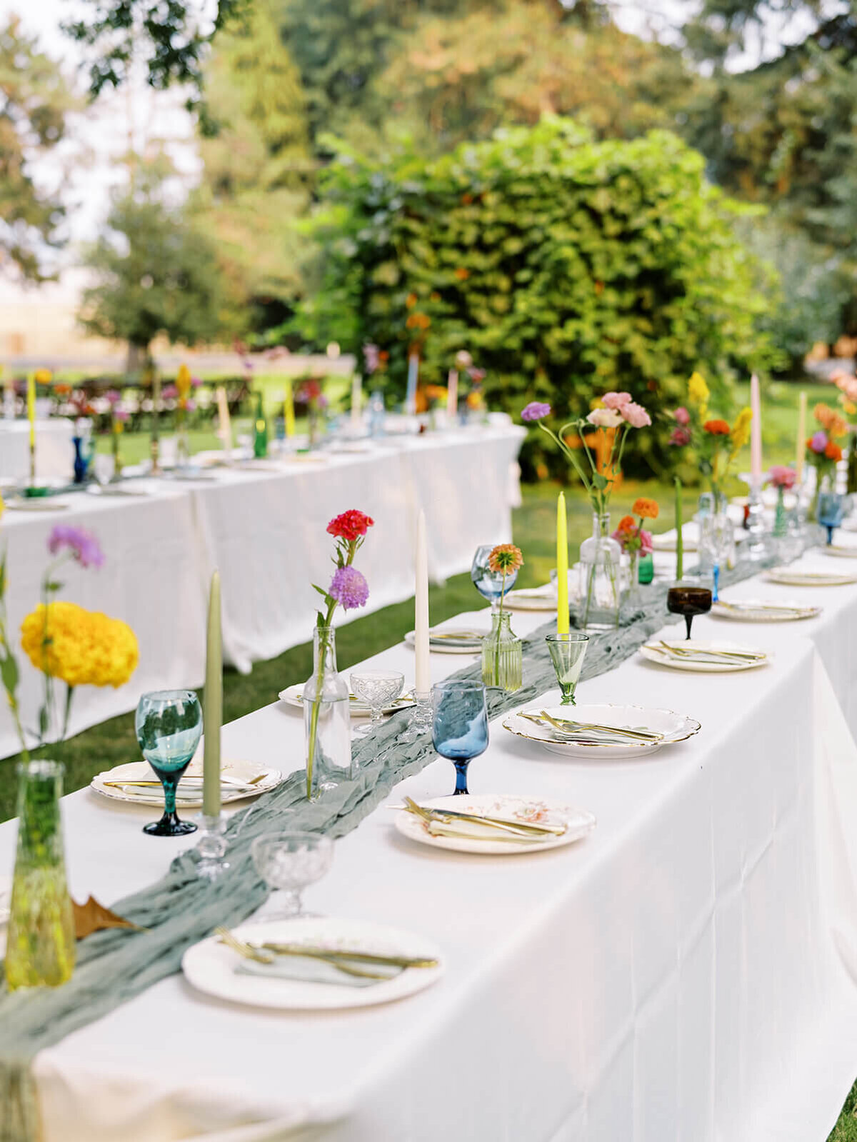 Outdoor wedding reception with tables set for guests with flowers and plates. 