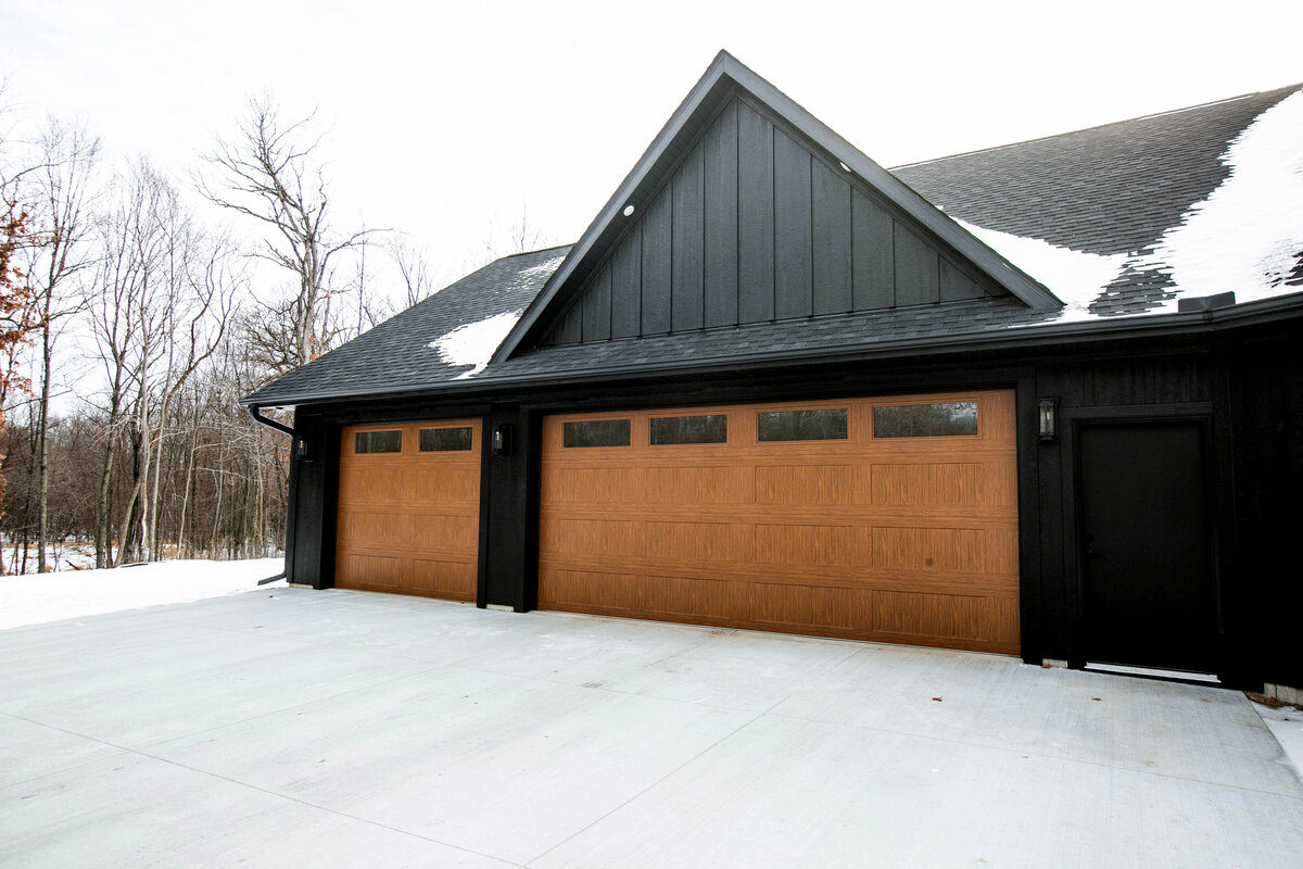 Exterior view of custom home in Elk River, Minnesota with black siding, wood details and front porch built by Cornerstone Custom Builds
