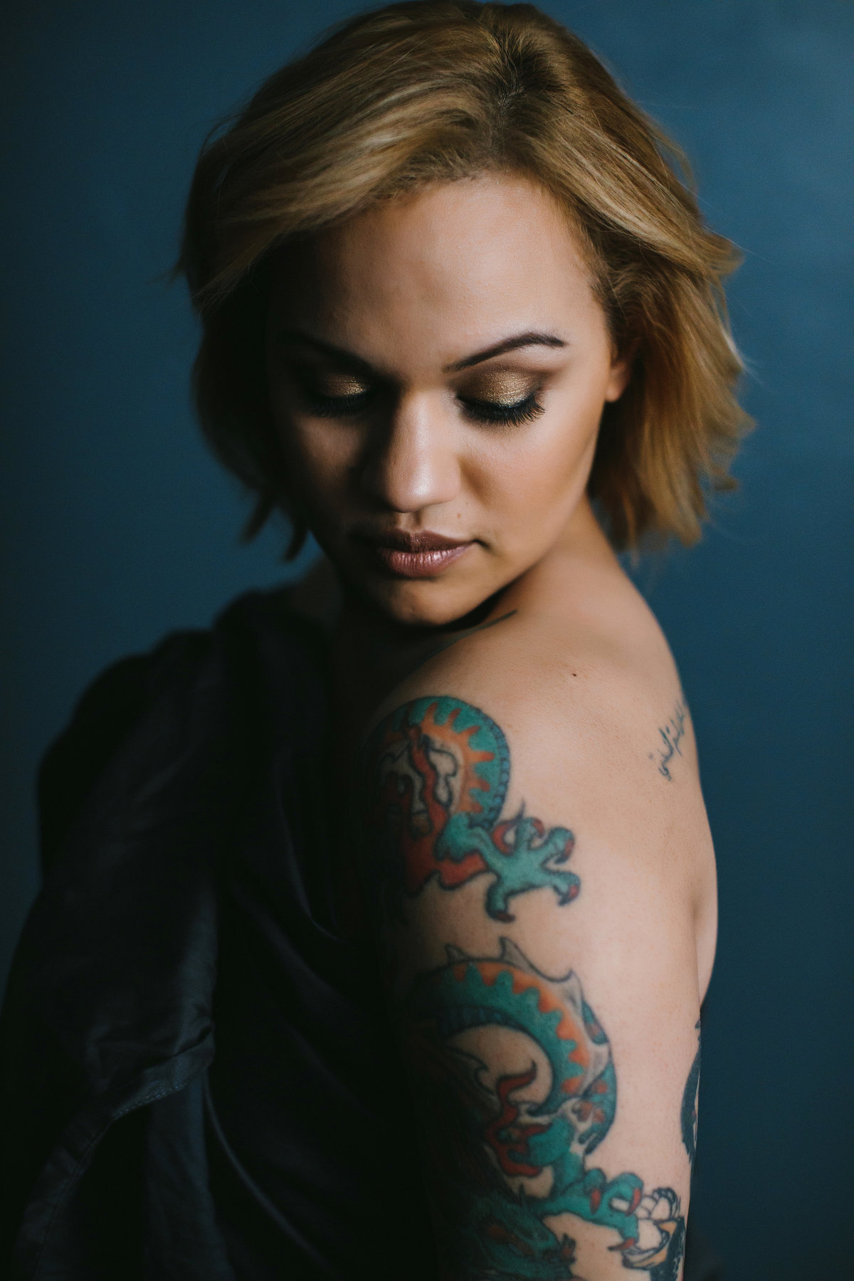 stunning boudoir portrait of woman with large tattoo posing against blue backdrop