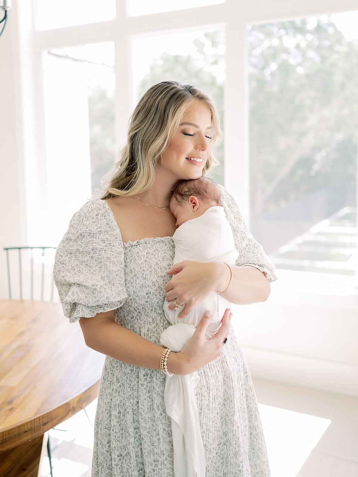 A tender moment as a mother holds her newborn close to her chest. The baby rests peacefully against her, wrapped in a soft blanket, while she gazes down with love and warmth. The soft lighting and gentle embrace capture the deep bond between mother and child