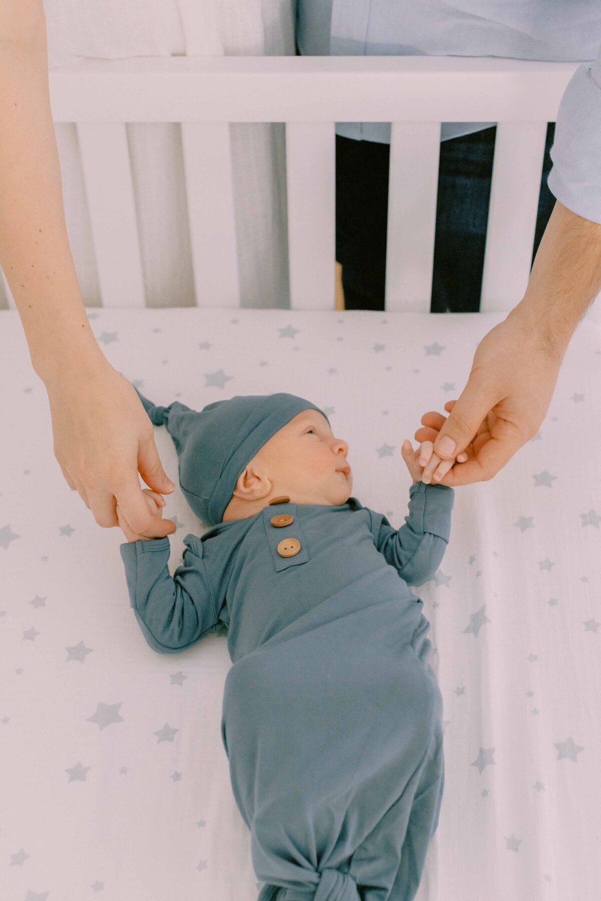 Baby laying in crib while parents hold both of his hands
