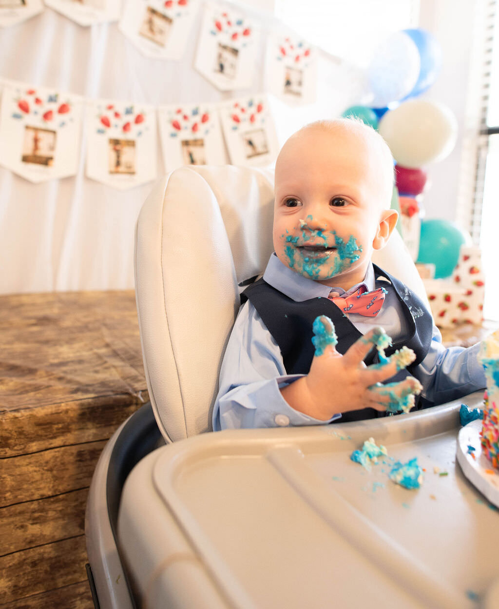 A baby smiling in a high chair covered in cake and blue frosting.