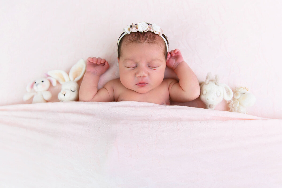 newborn girl laying on her back on a white backdrop with tiny stuffies for her newborn photography session in Burlington, Ontario