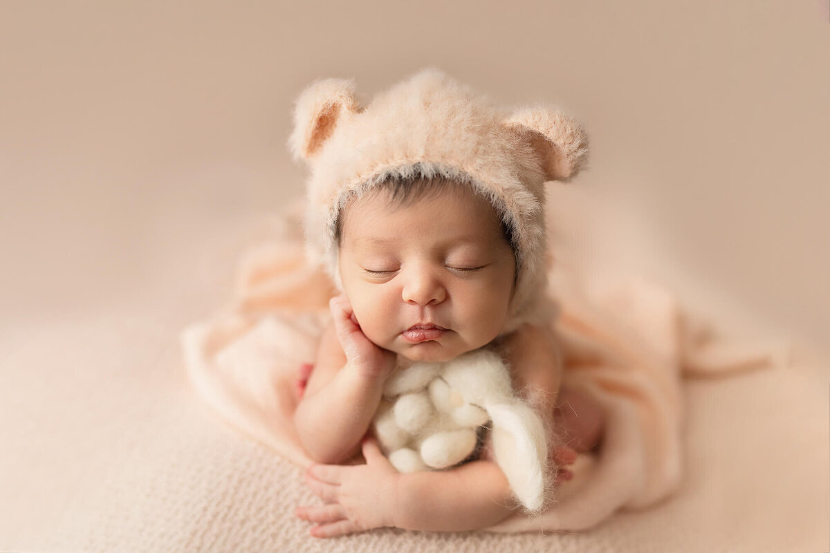Newborn girl with bonnet posed with small white bunny lovey.