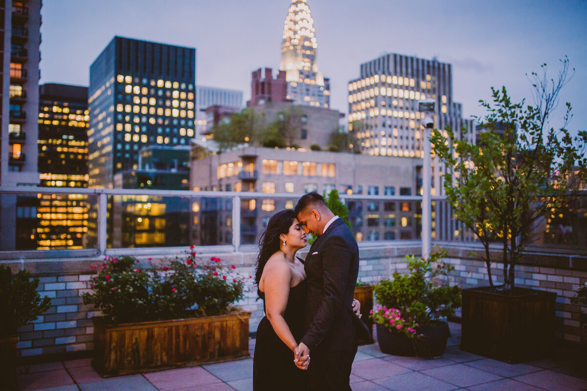 A couple holding hands on a rooftop in new york city in the evening wearing black formal outfits at night