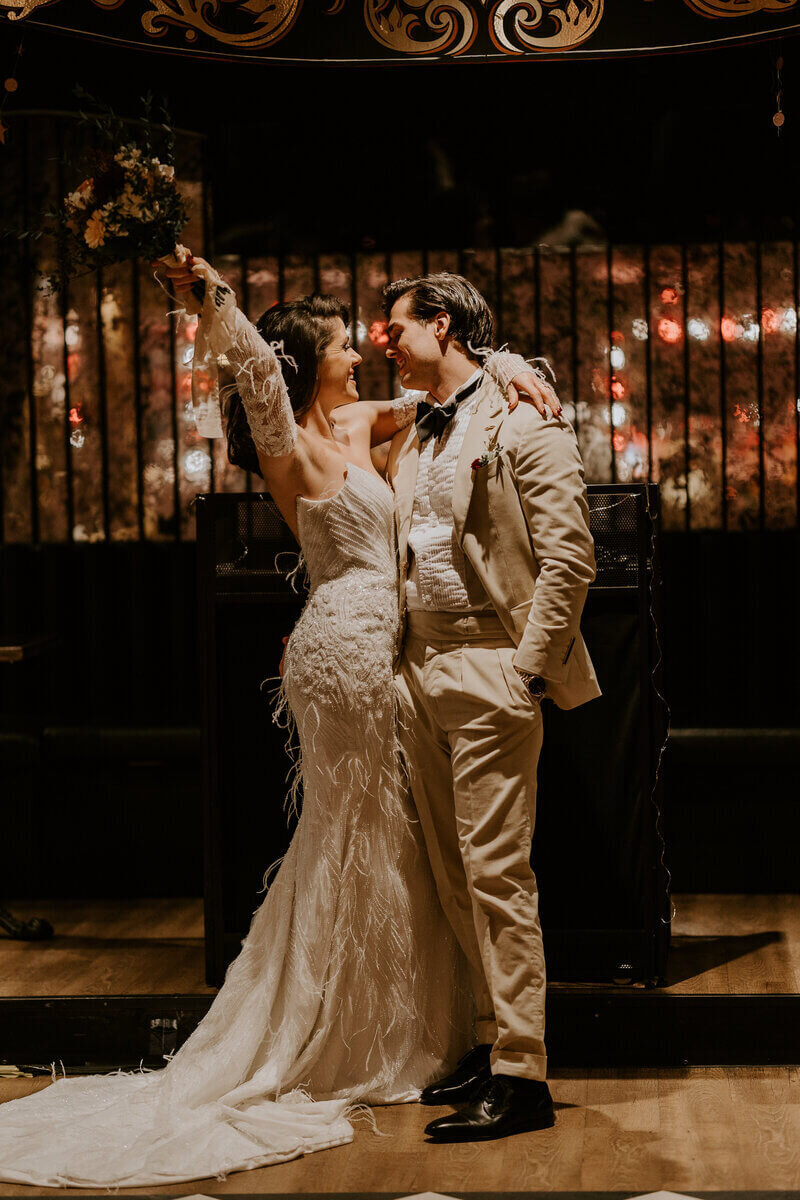 Marié bras entourant la taille de la mariée, qui brandit son bouquet de fleurs, dans un décor vintage immortalisés par Laura Termeau photographie.