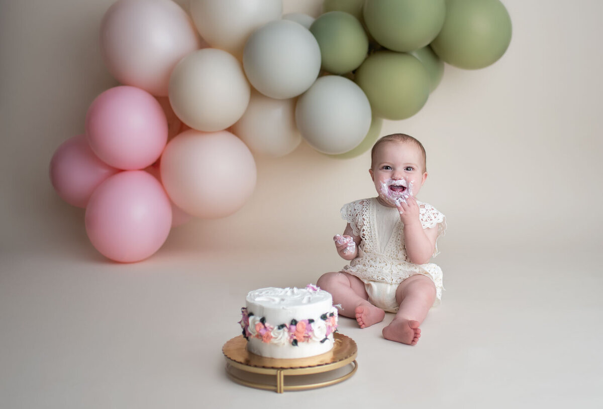 smiling baby eating a cake with flowers at her st. louis cake smash session