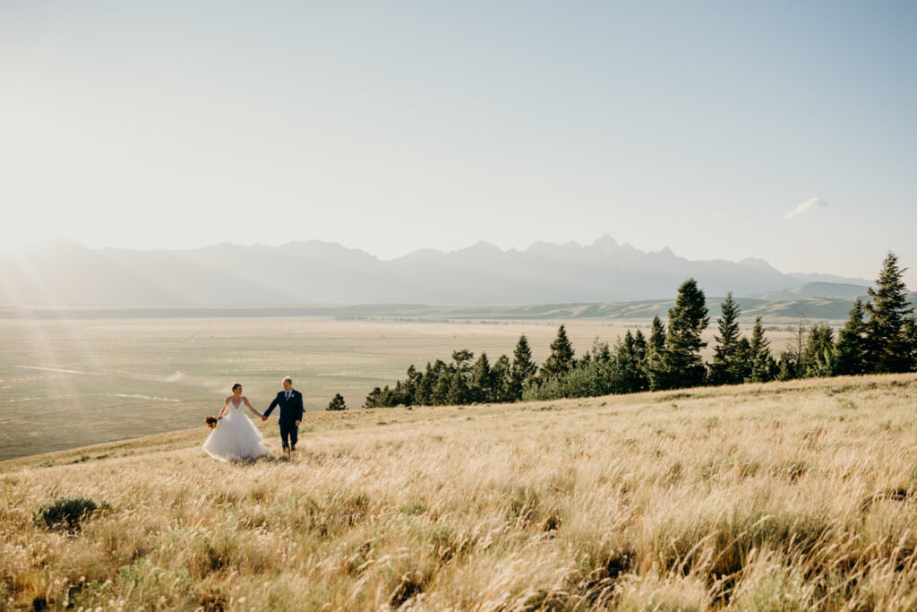 Curtis Canyon Campground wedding location for grand teton wedding with bride adn groom running up a hill together while the sun shines over the golden field of fall grasses captured by jackson hole photographers