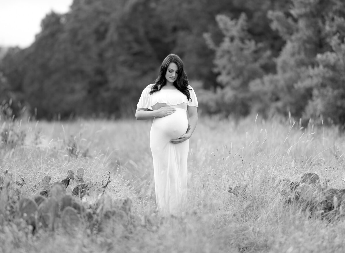 pregnant woman wearing white looking down at her belly