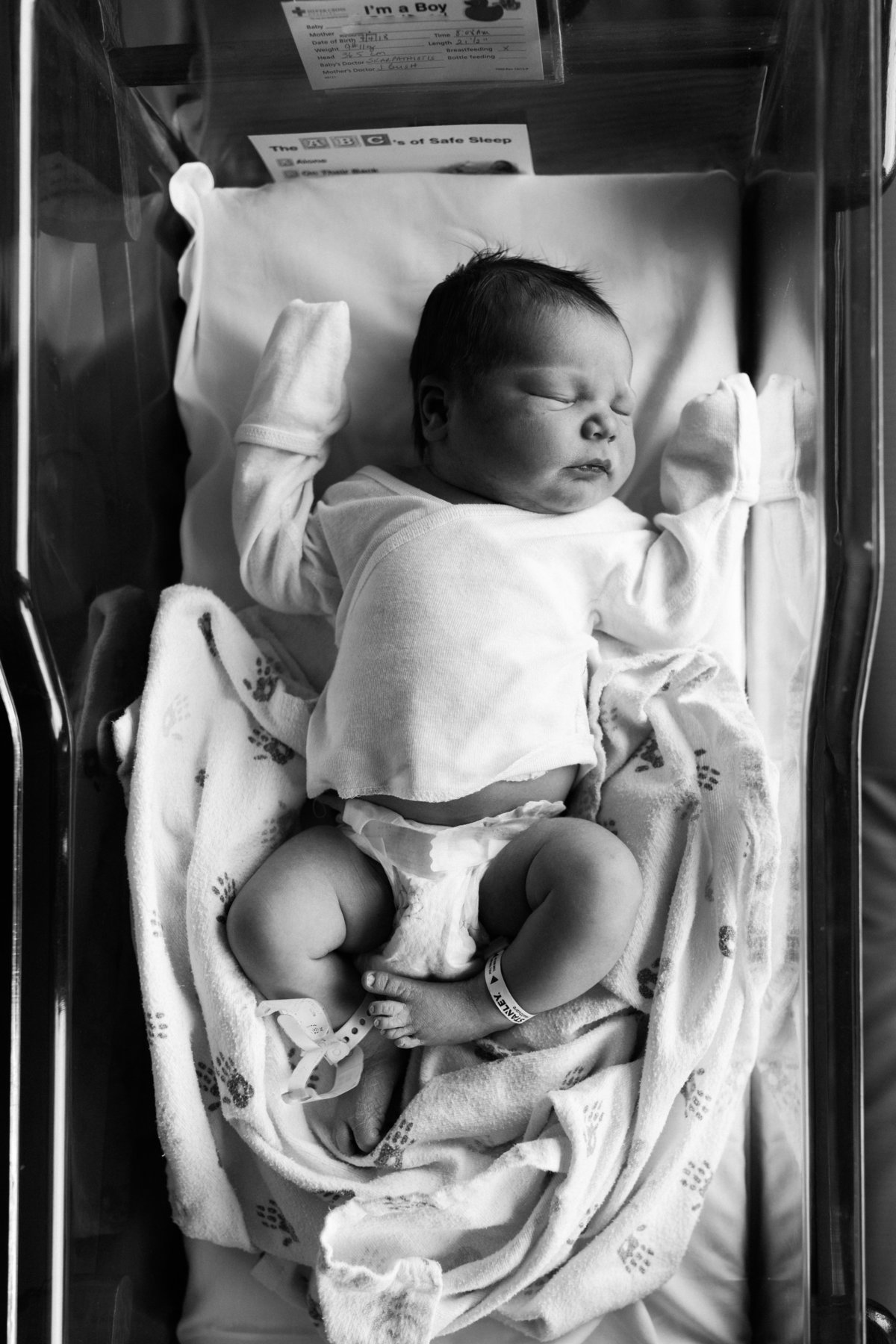 Black and white image of newborn baby girl in hospital bassinet