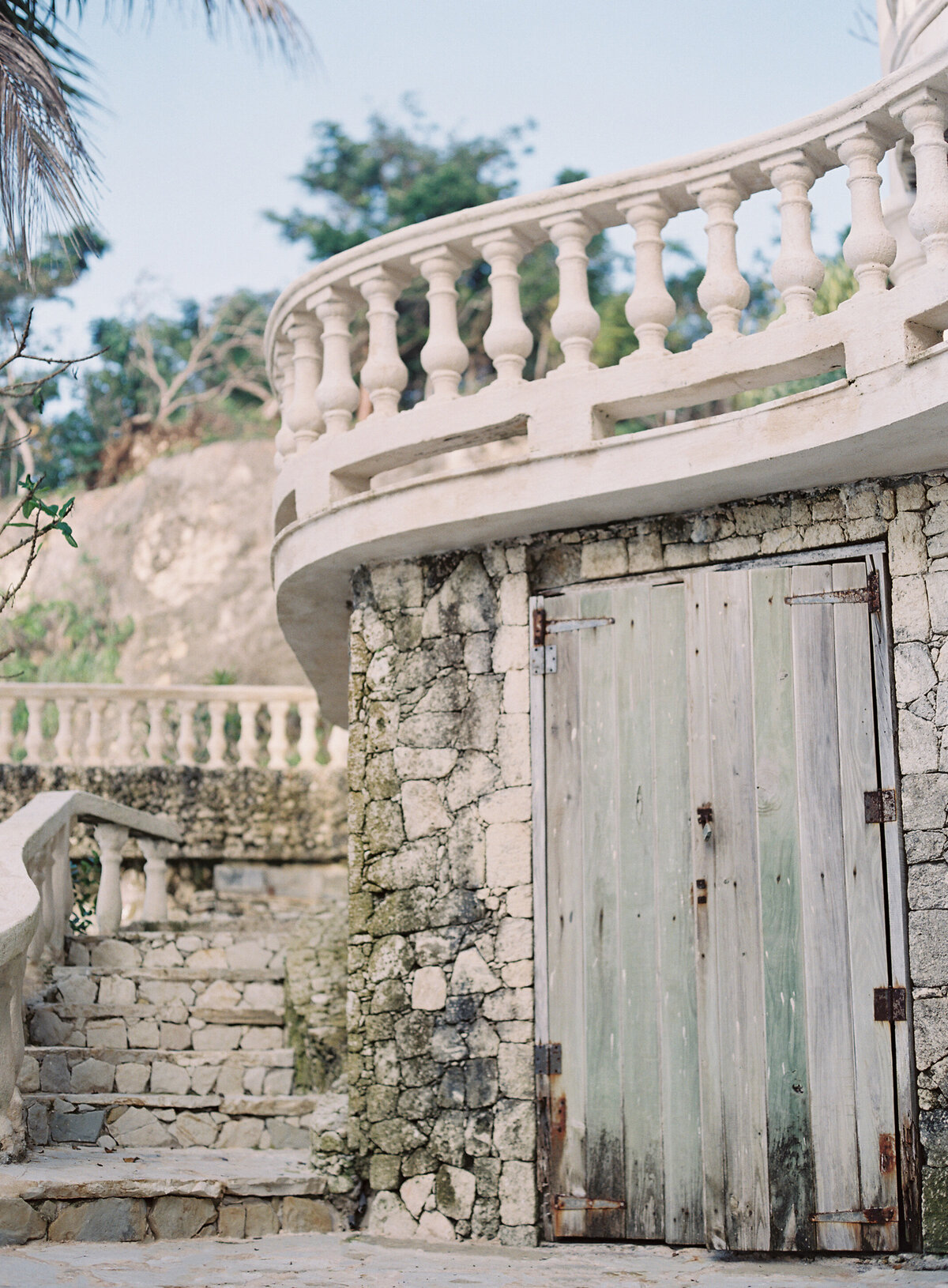 A romantic Caribbean destination wedding scene captured by photographer Laura Gordon. A beautiful bride in a lace wedding dress and her groom in a suit and bow tie, stand closely together in the Dominican Republic. The groom holds the bride's hand as they gaze at each other, bathed in soft sunlight, creating a dreamy tropical ambiance.