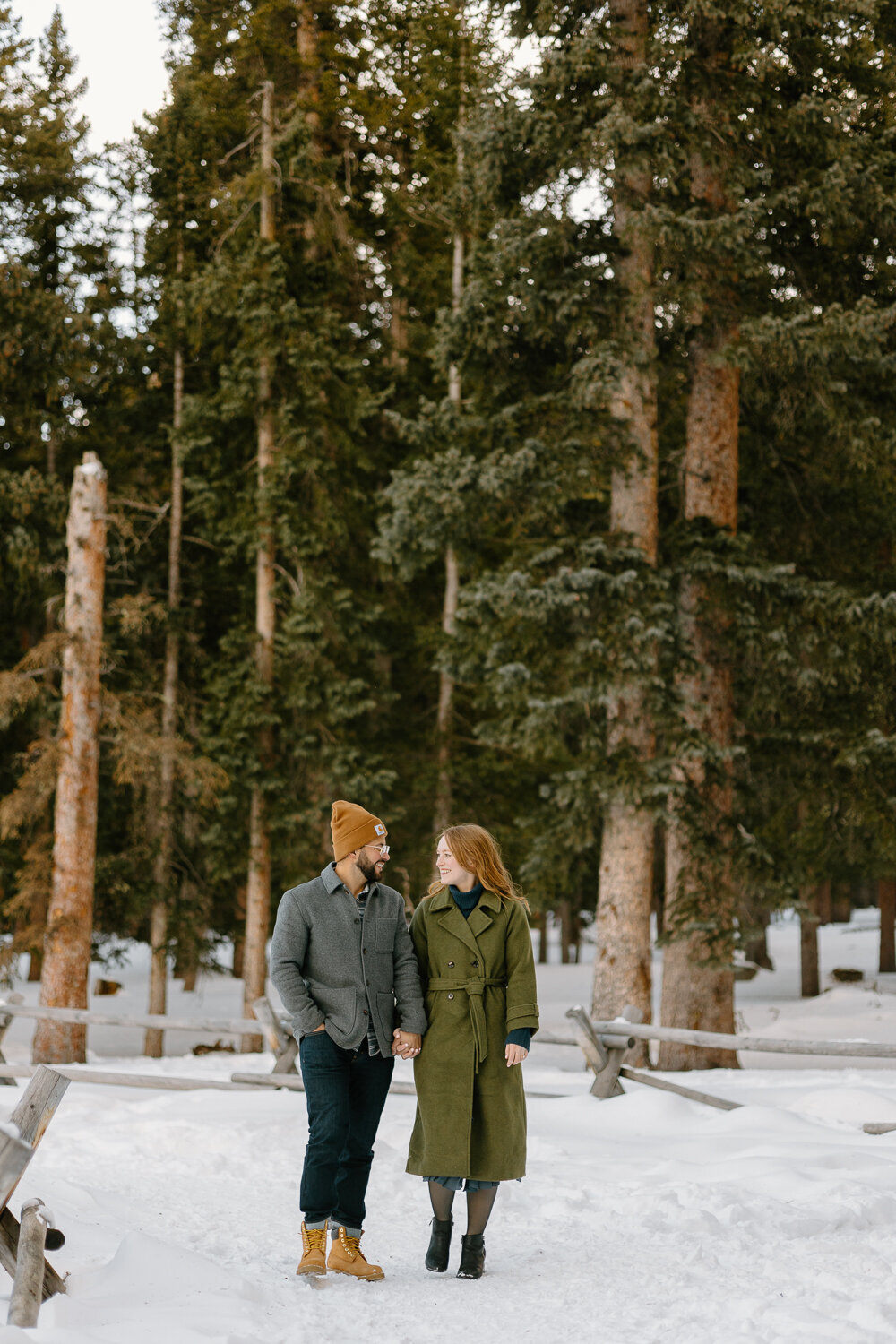A young couple holds hands and walks through the forest during their engagement session in Denver, Colorado.