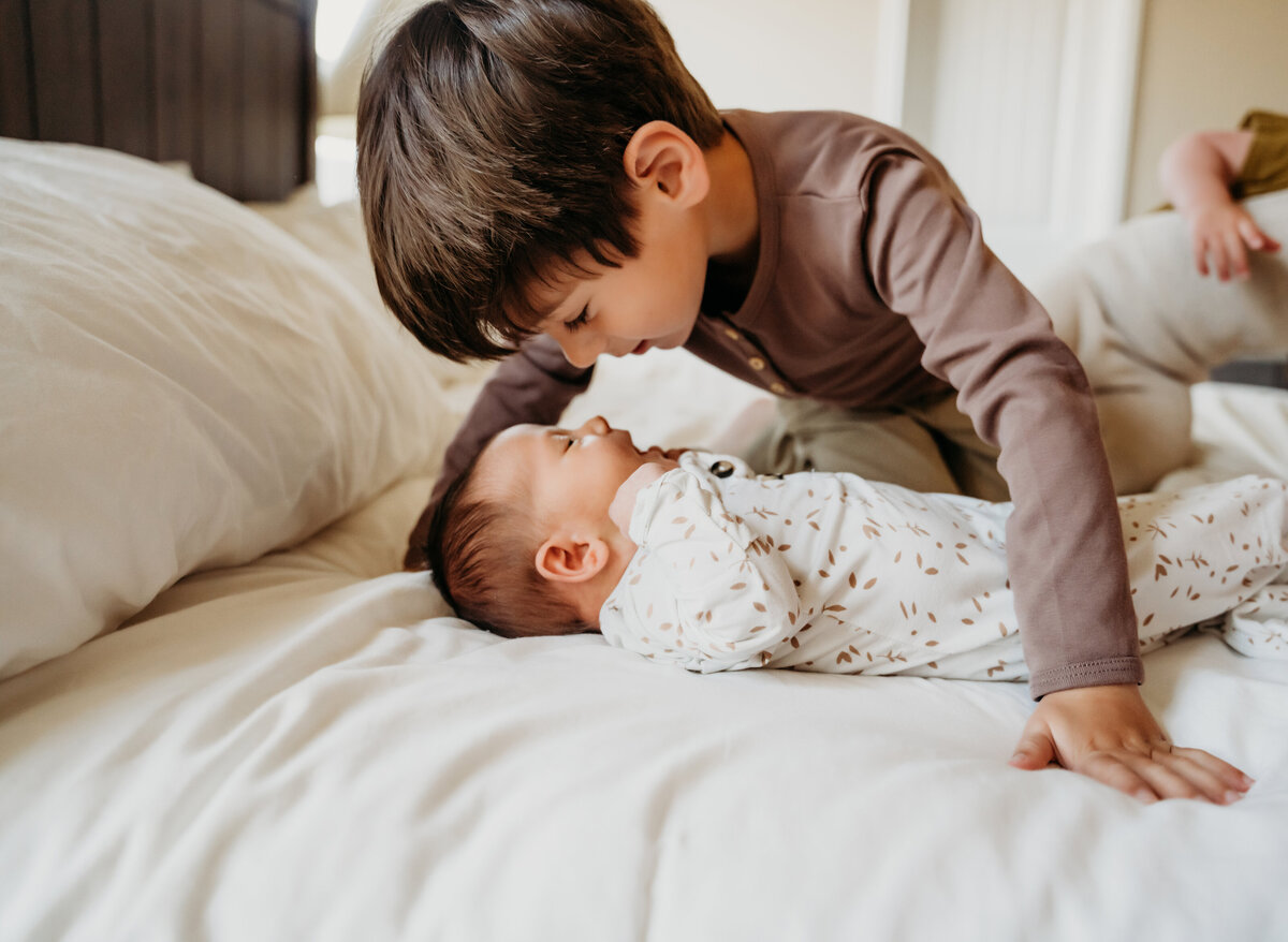 Newborn Photographer, a young boy admires his little baby brother laying on the bed
