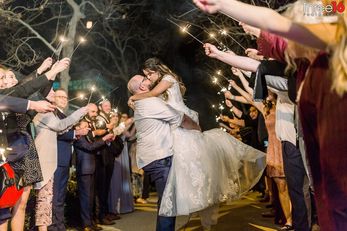 Groom lifts his Bride in the air and kisses her during their grand exit under a tunnel of sparklers