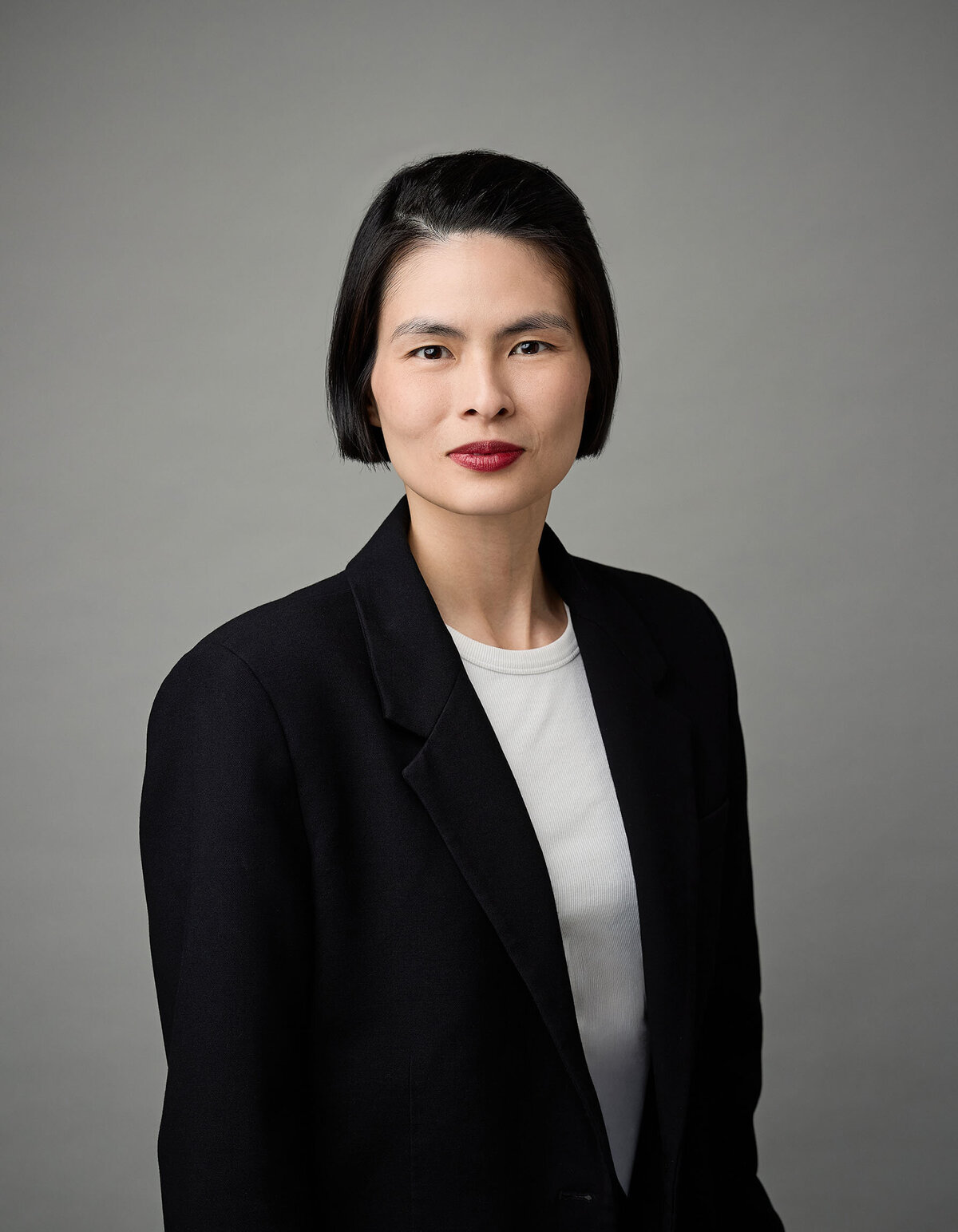 Elegant portrait of a woman with a jet black bob, red lipstick and alabaster skin.  She's wearing a back jacket and white tshirt.
