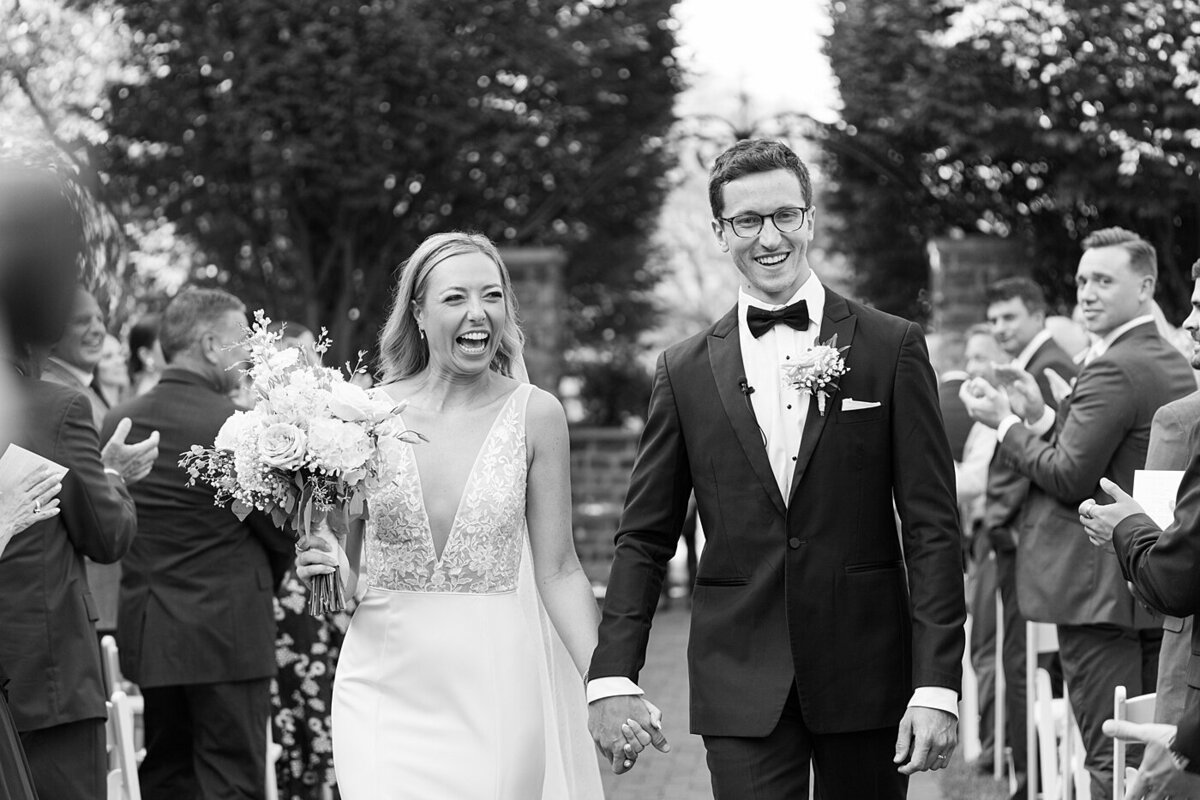 Columbus wedding  photographer  photographs wedding ceremony exit with bride and groom holding hands and smiling while their guests clap for them in celebration