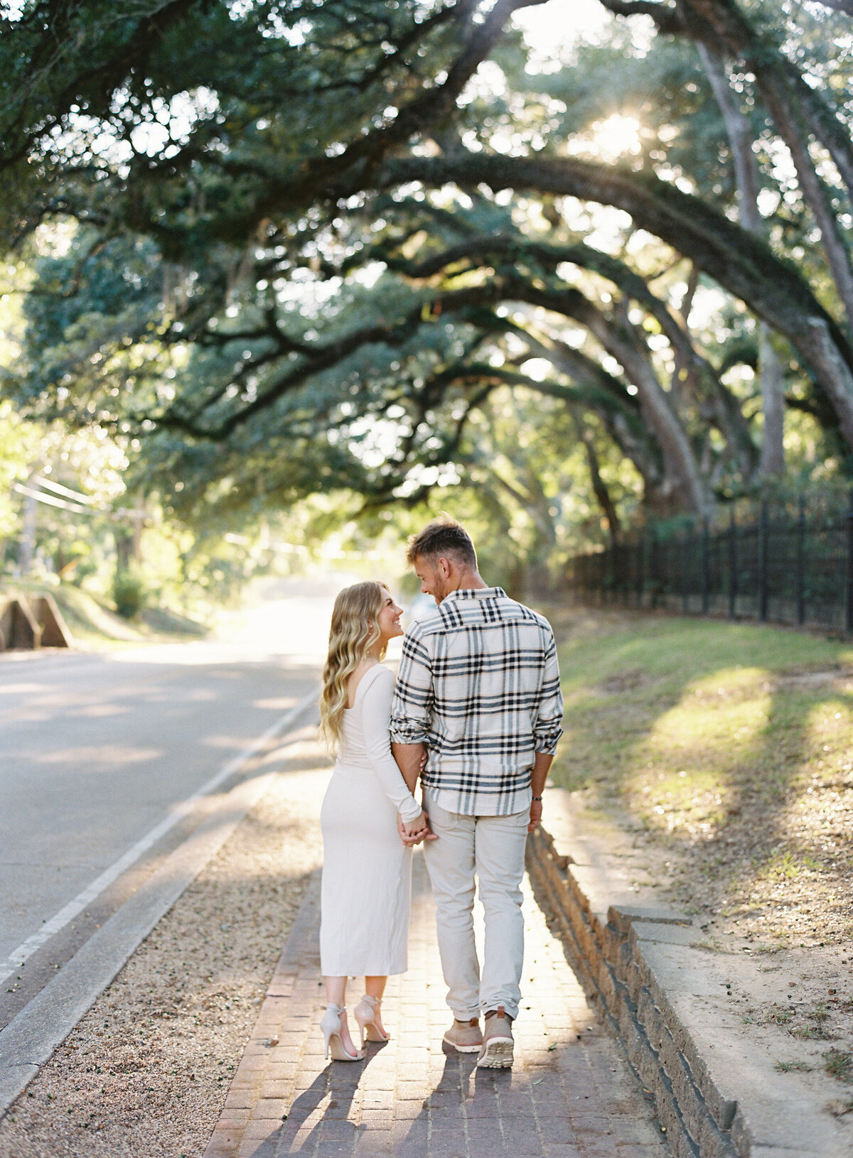 Couple enjoying a romantic engagement session under the oak trees in downtown Saint Francisville, LA, captured on film by Morgan Alysse, Louisiana film photographer.