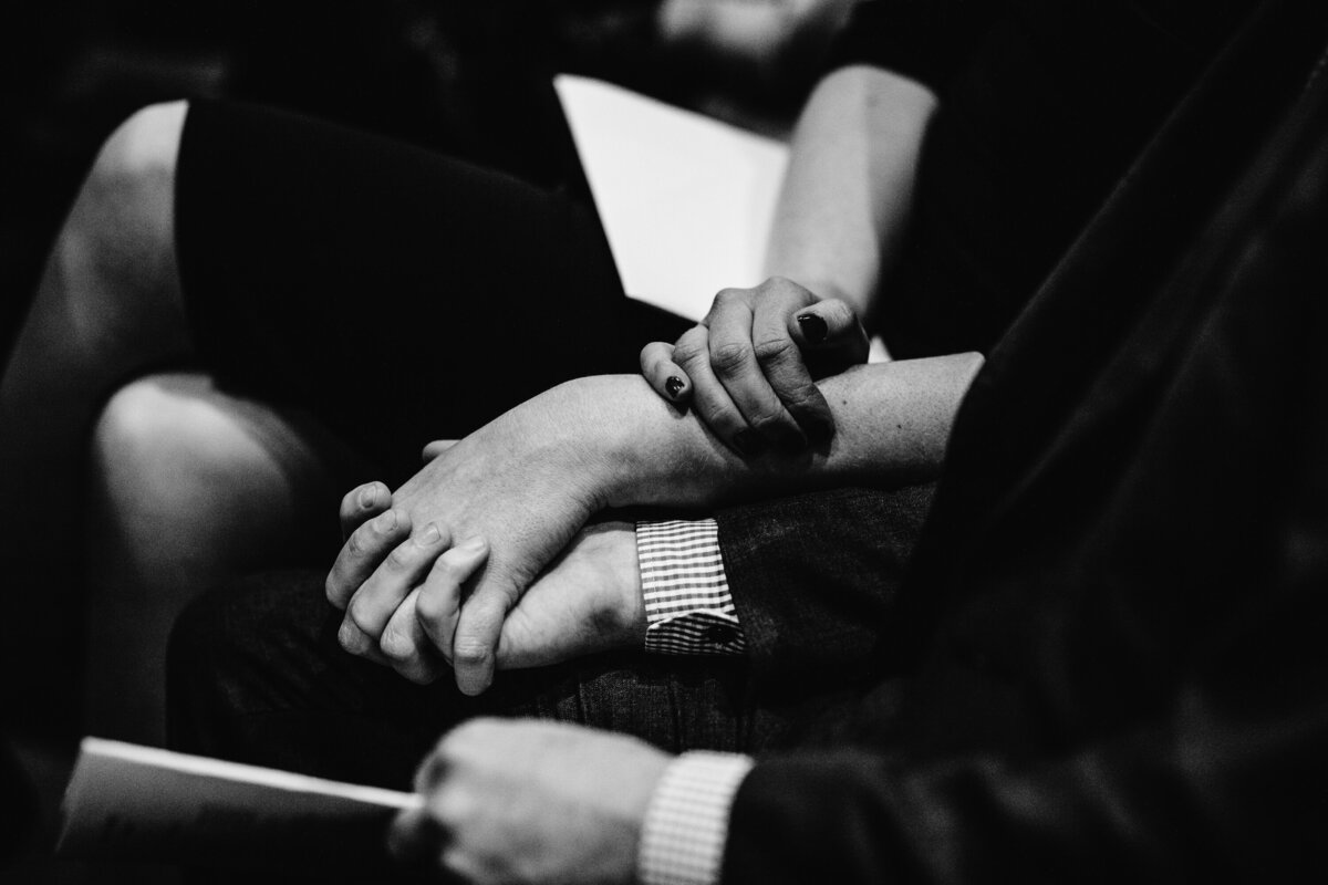 Black and White detail shot of wedding guest holding hands in church pews