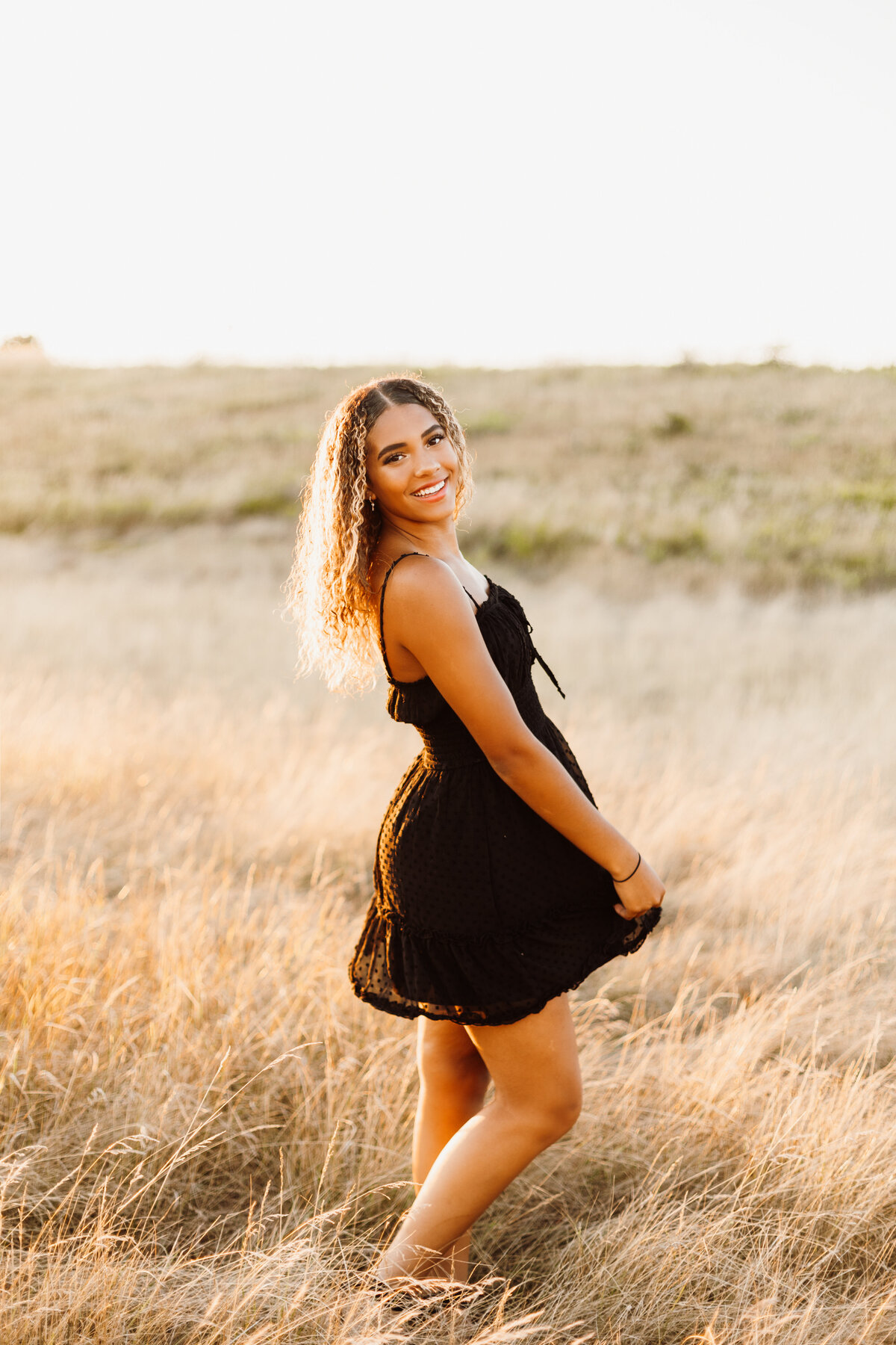 Senior girl in a black dress twirling in a yellow grassy field