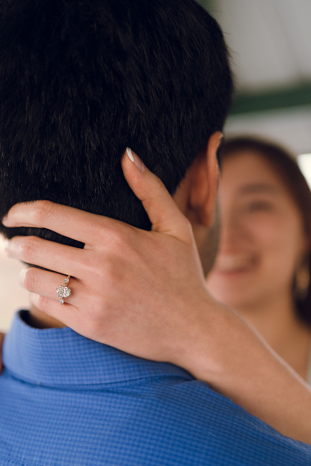 engagement ring close up with woman smiling in the background