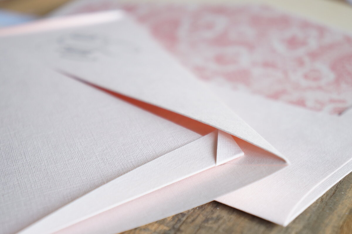 Corner of an origami wedding invitation with pink paper and pink envelope