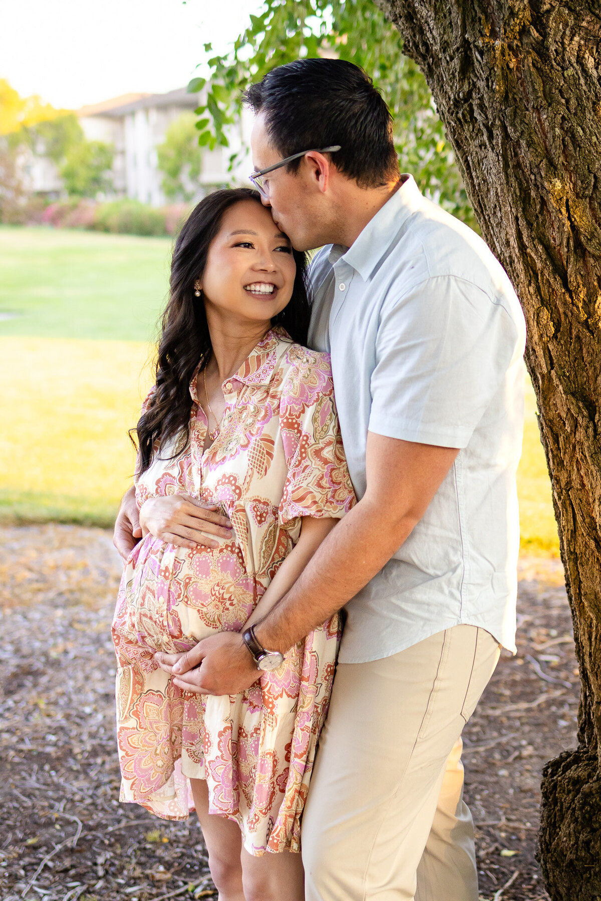 Expecting couple embraces under a tree at sunset as the father kisses the mother’s forehead — Bay Area Maternity Portfolio - Ellobelle Photography.