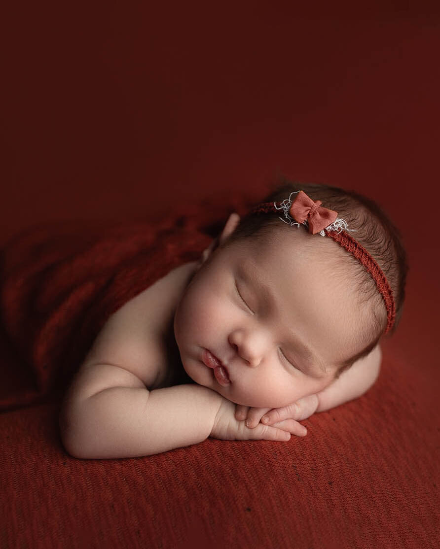 A newborn baby sleeps in a red headband and blanket on a matching pad