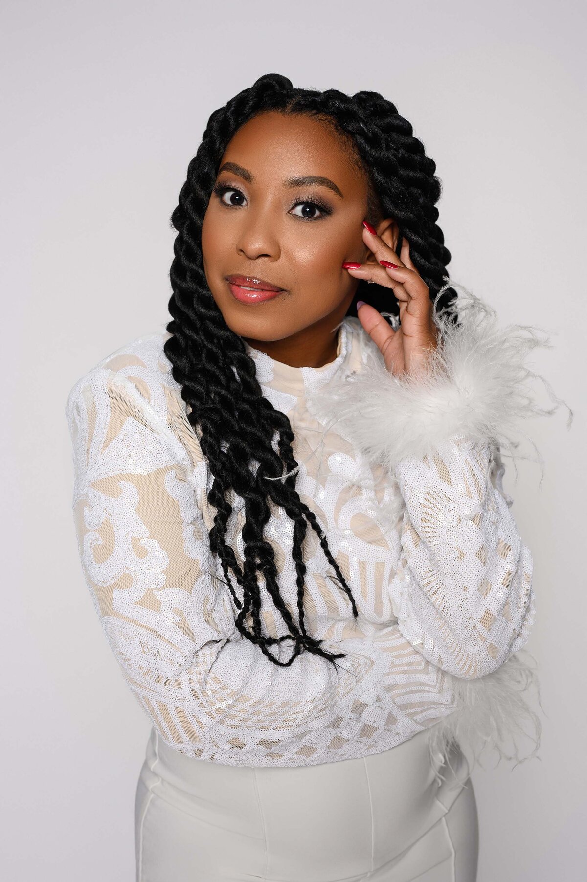Woman in a white lace dress with feather details, posing with her hand near her face