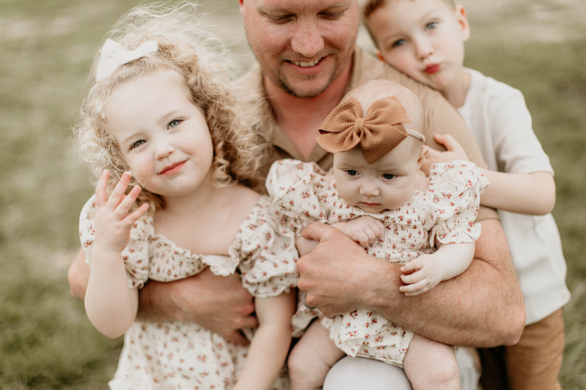 Natural light photo of dad kneeling with his kids by a tree. 