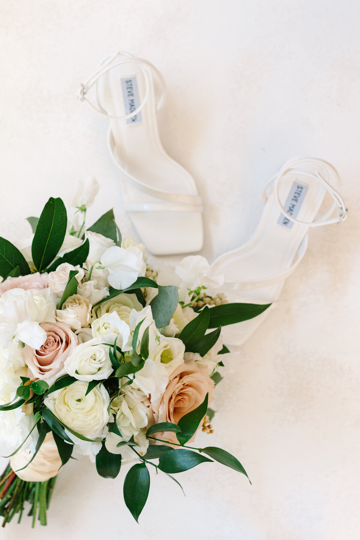 bride's shoes with a white, soft pink, and loose greenery wedding bouquet.