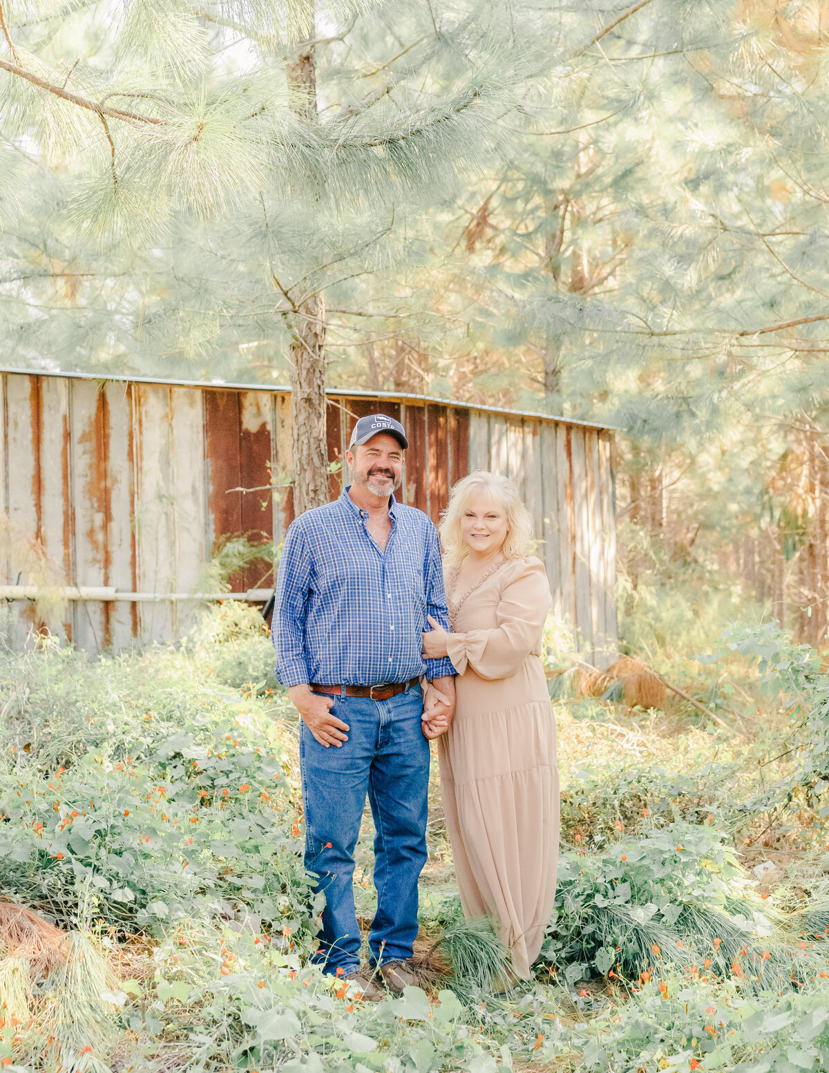 grandparents standing in grass in front of their barn with grandmother holding grandfather's arm