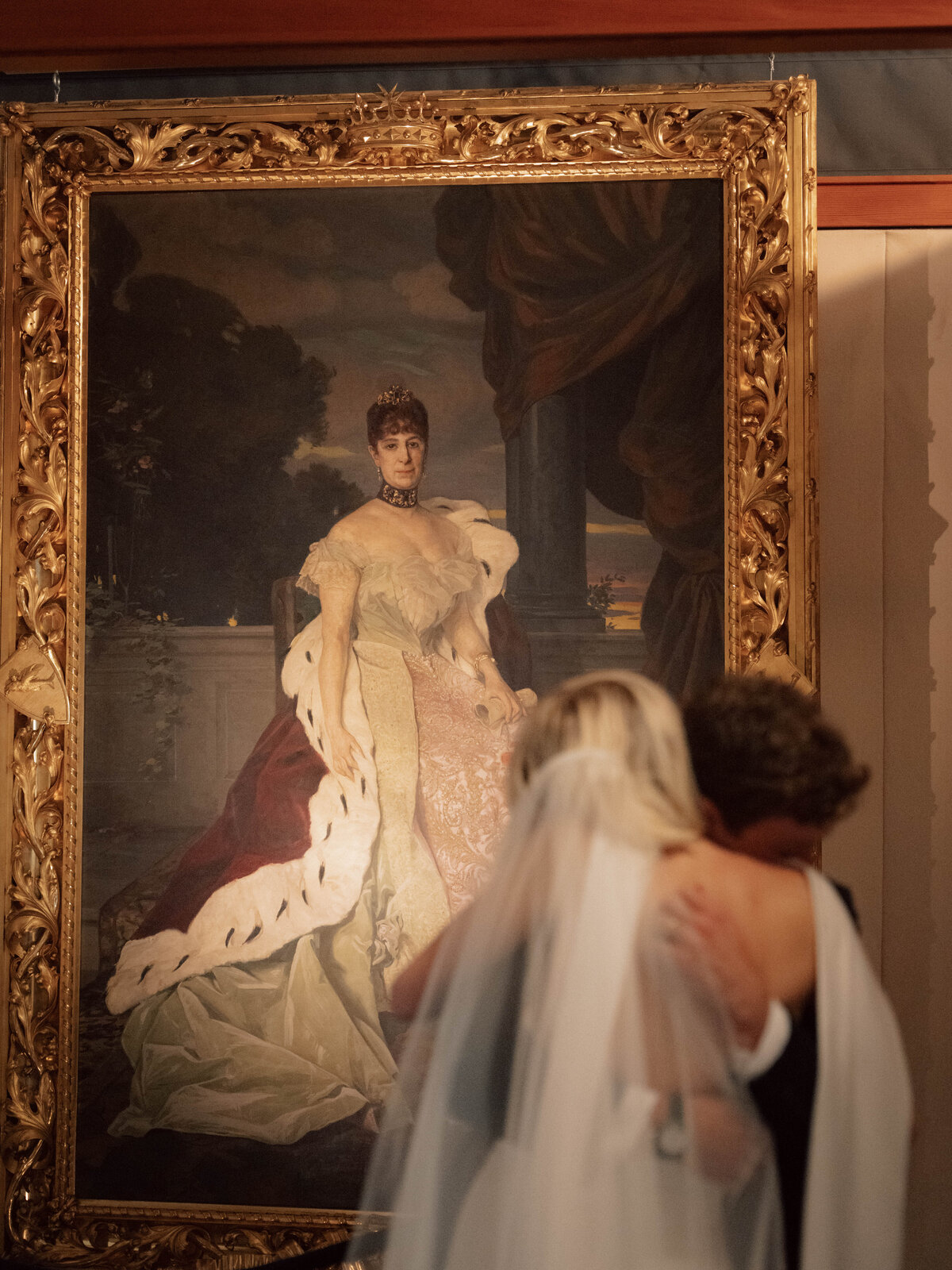Bride and groom embrace during emotional wedding moment in front of framed portrait
