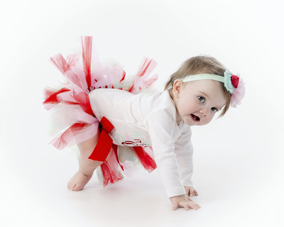 A little girl wearing a colorful tutu crawls across an Iowa Milestone Photographer’s Studio