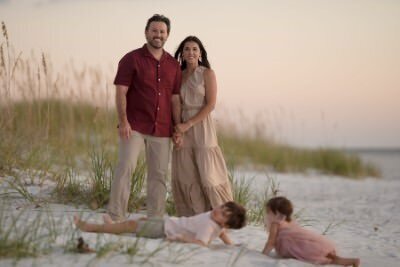 Beautiful sunset family photo session on St Augustine beach with parents standing while children play in sand, captured by professional family photographers