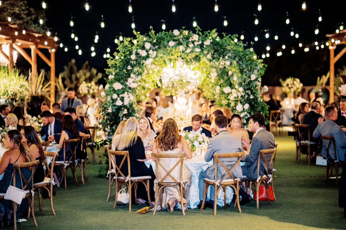 A beautifully decorated wedding reception with lush floral centerpieces, candlelit tables, and a romantic ambiance set under the night sky.