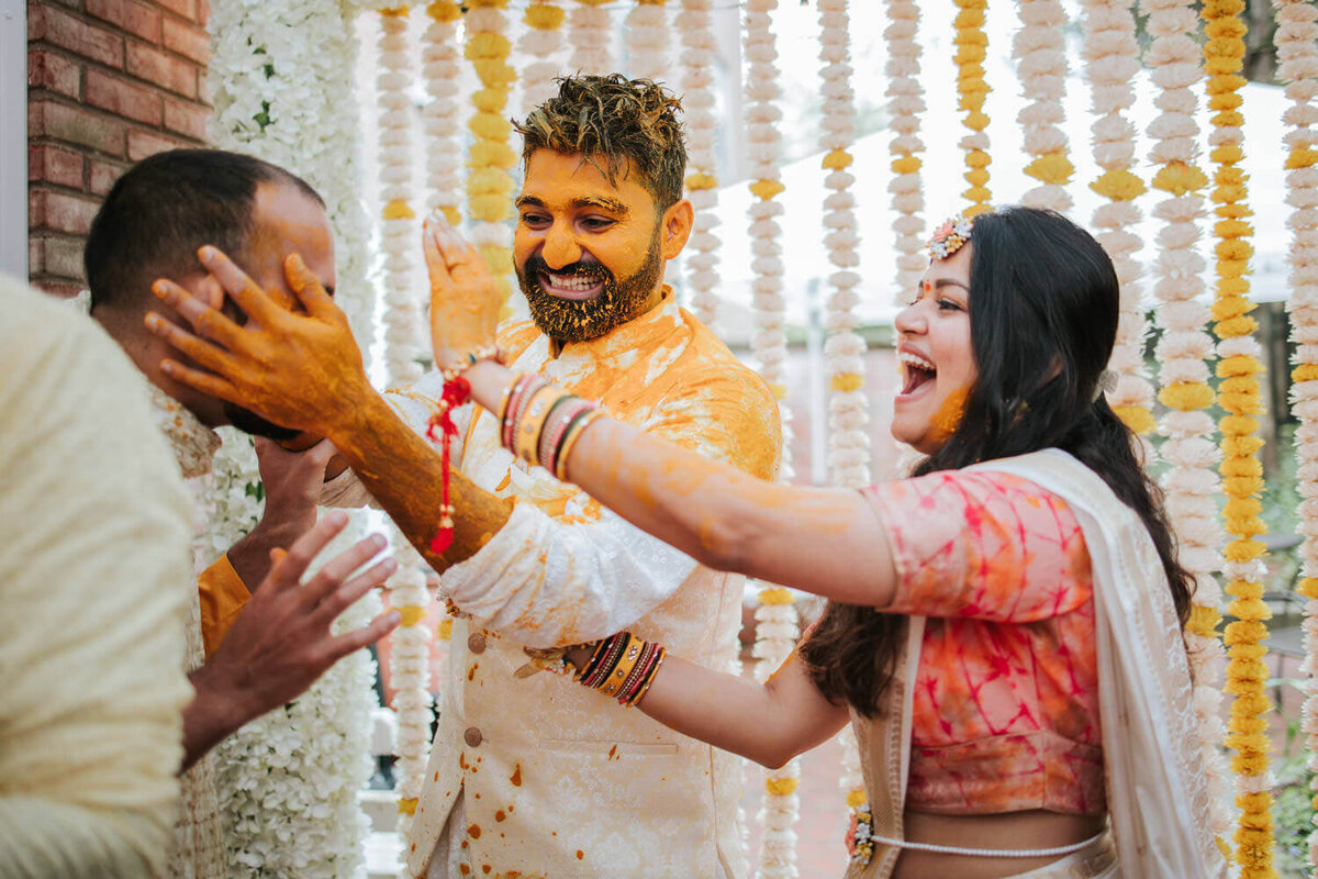 A joyful couple celebrates during a vibrant Haldi ceremony, surrounded by marigold garlands and laughter.