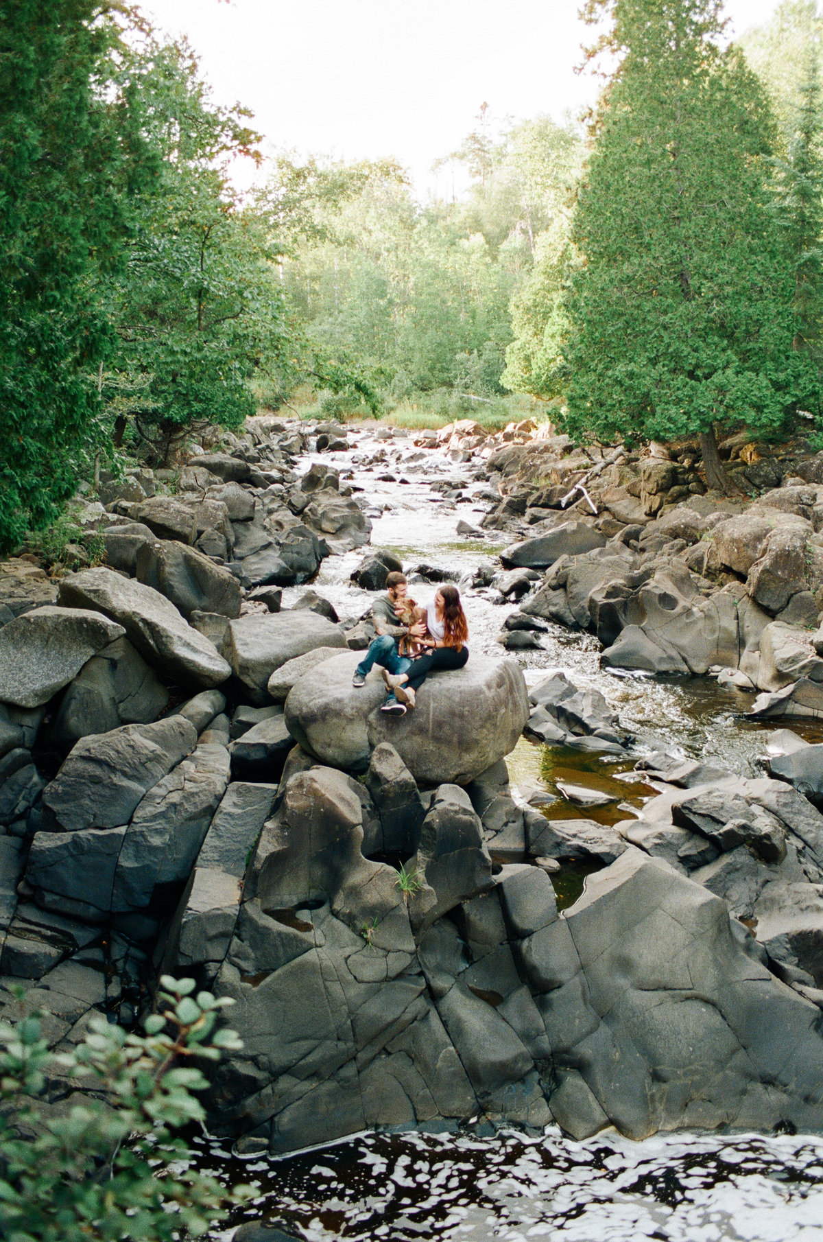 wide shot of couple and dog sitting on tall boulders in river of minnesota state park