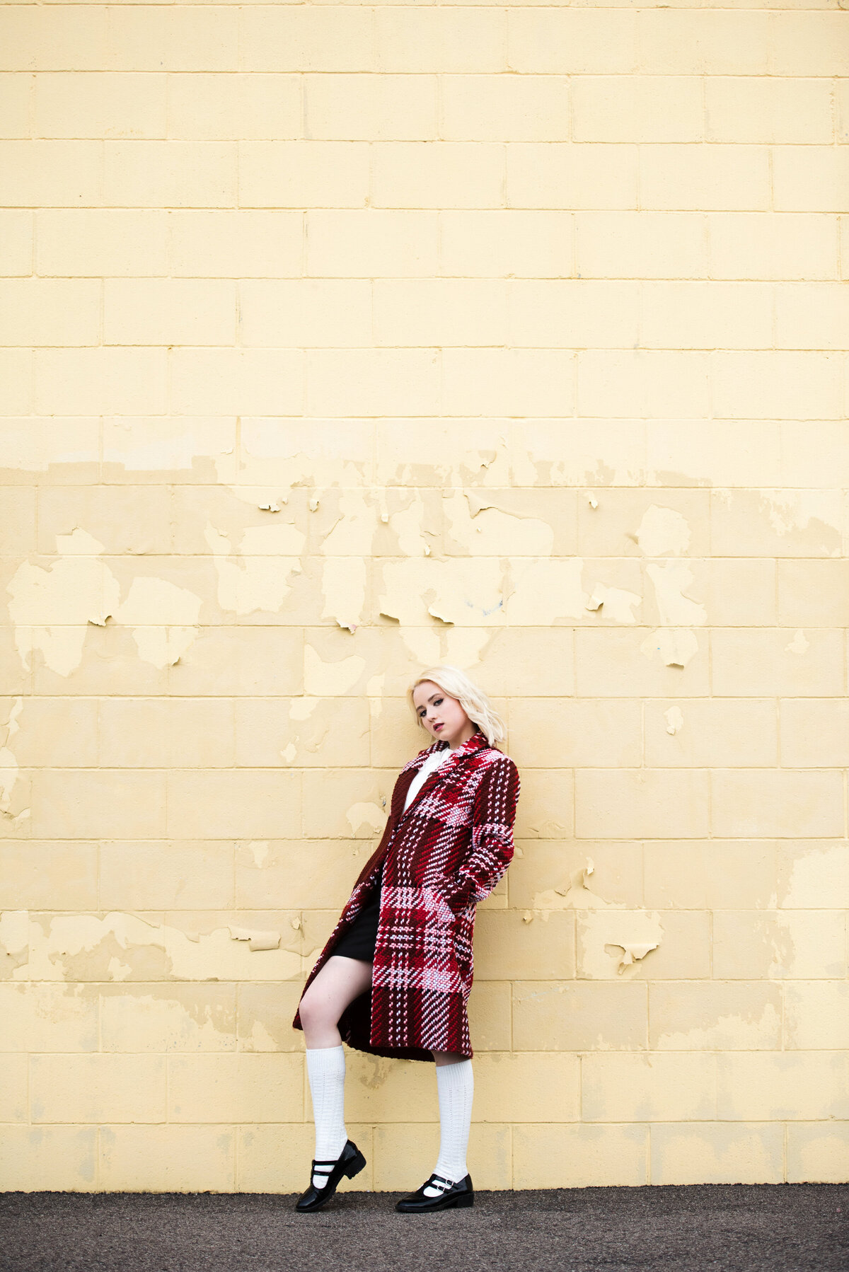 high school senior girl in plaid jacket leaning against yellow wall