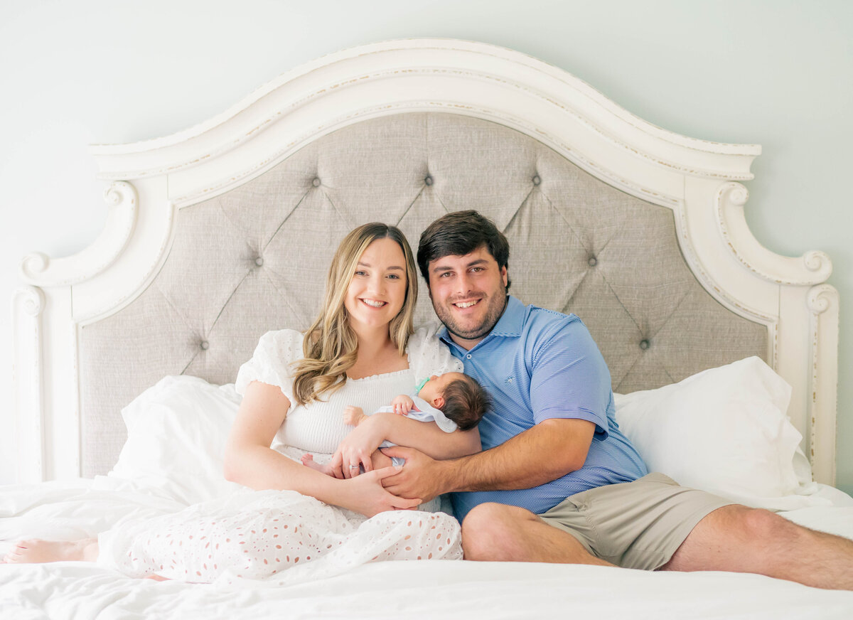 proud mom and dad with their newborn baby sitting on their bed during their indoor shoot