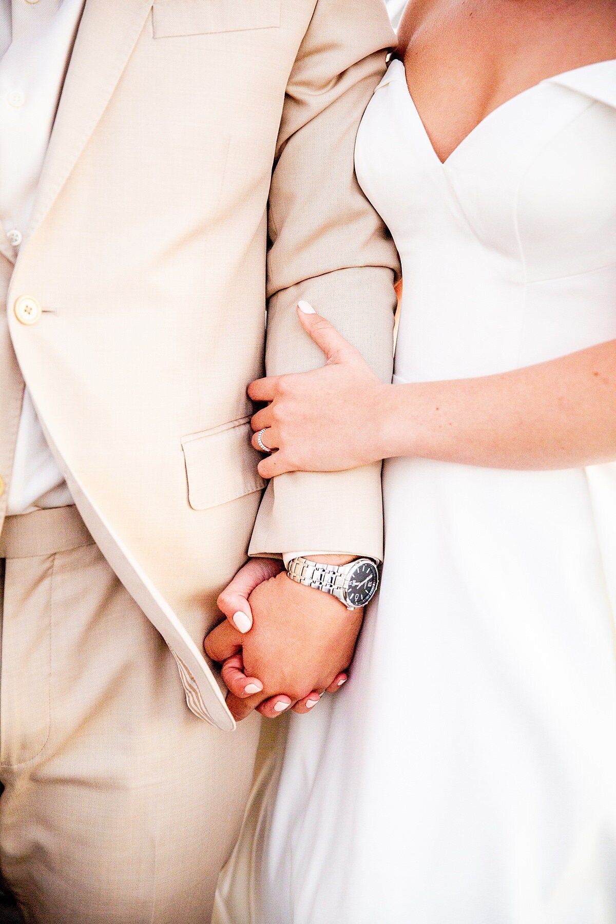 Groom in tan suit and bride in white gown holding hands