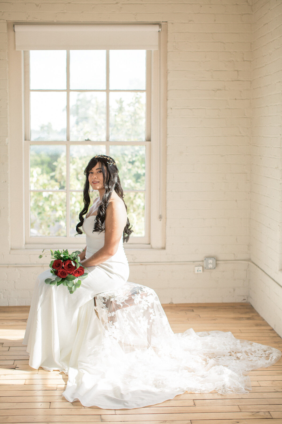 The seated bride smiles at the camera, showcasing a gorgeous lacy veil a bouquet of red roses.  Photographed by Stephanie Eddy, Colorado wedding photographer