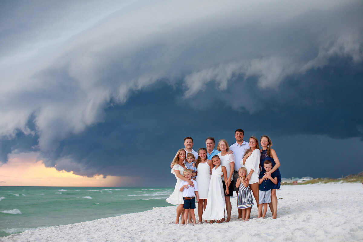 Smiling happy family posing together on the white-sand beach in front of a crazy storm cloud at Grayton Beach, Florida.  https://gwynegrayphotography.com