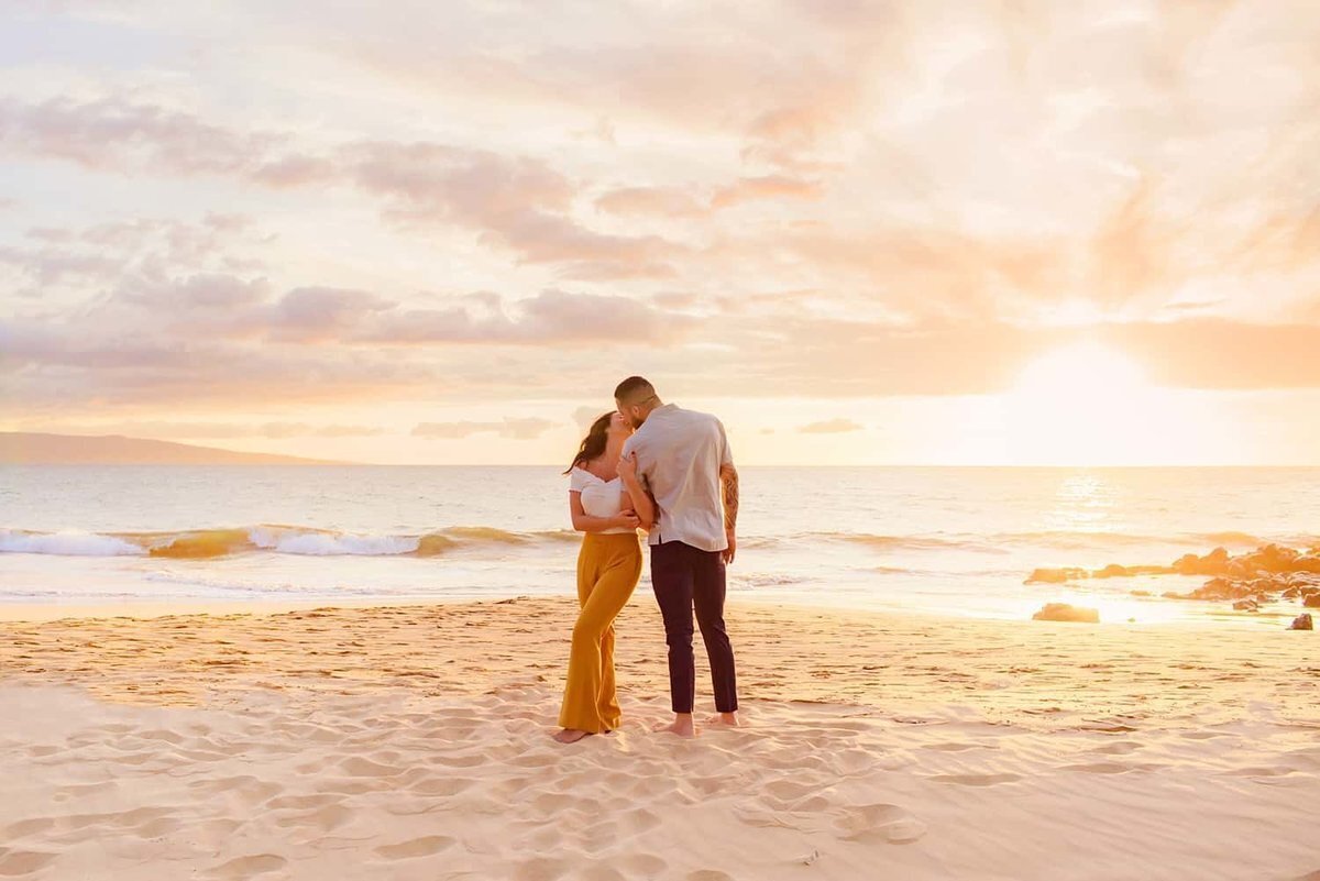 Woman wearing mustard yellow pants holds her boyfriend's arm after his Maui proposal on the beach