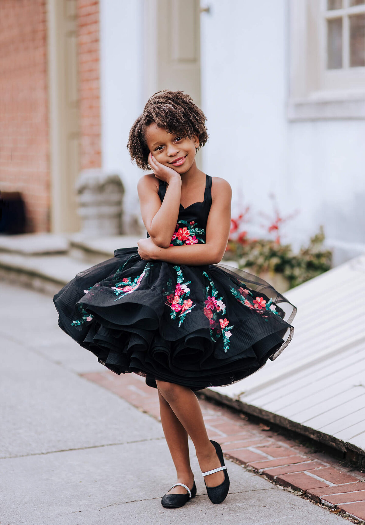 African American Girl wearing a black floral dress and black shoes with a hand on her cheek on a city street in Fells Point Baltimore Maryland