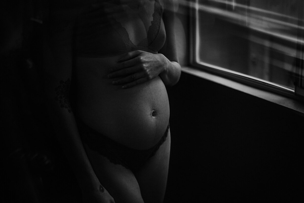 Woman with pregnant belly standing near a window letting light cast on her baby belly