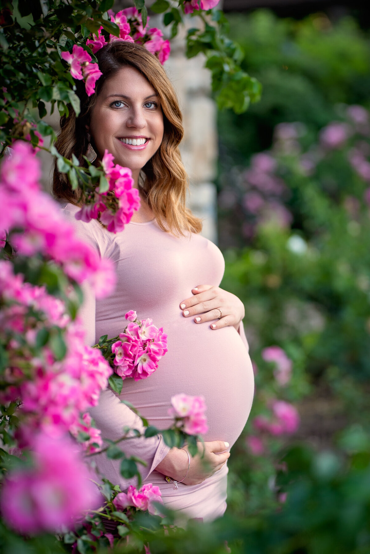 Whimsical maternity portrait surrounded by vibrant pink flowers in Leawood, Kansas. A stunning example of outdoor maternity photography for families in the Kansas City area.