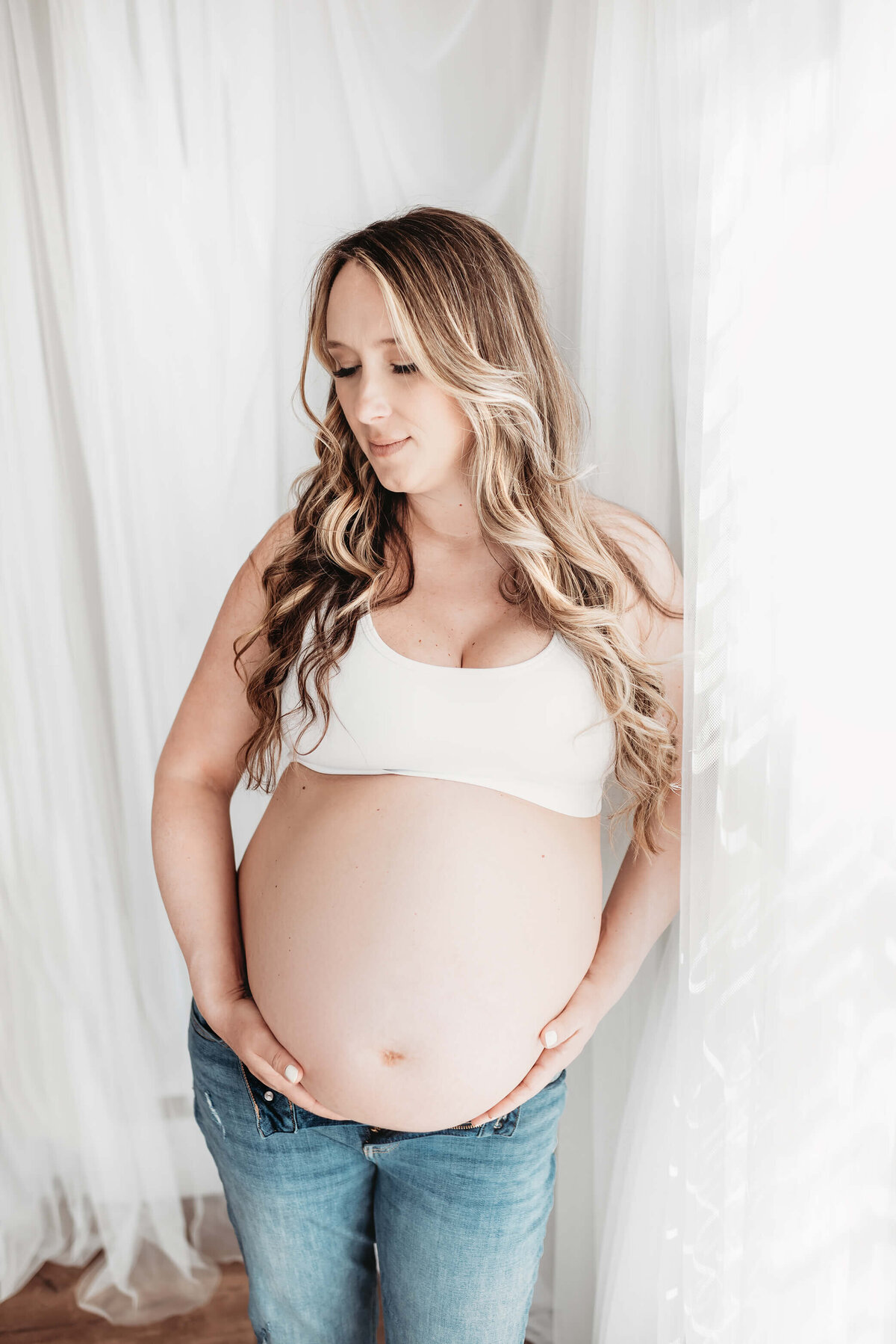 pregnant mother leaning against white curtains in denver maternity photography studio