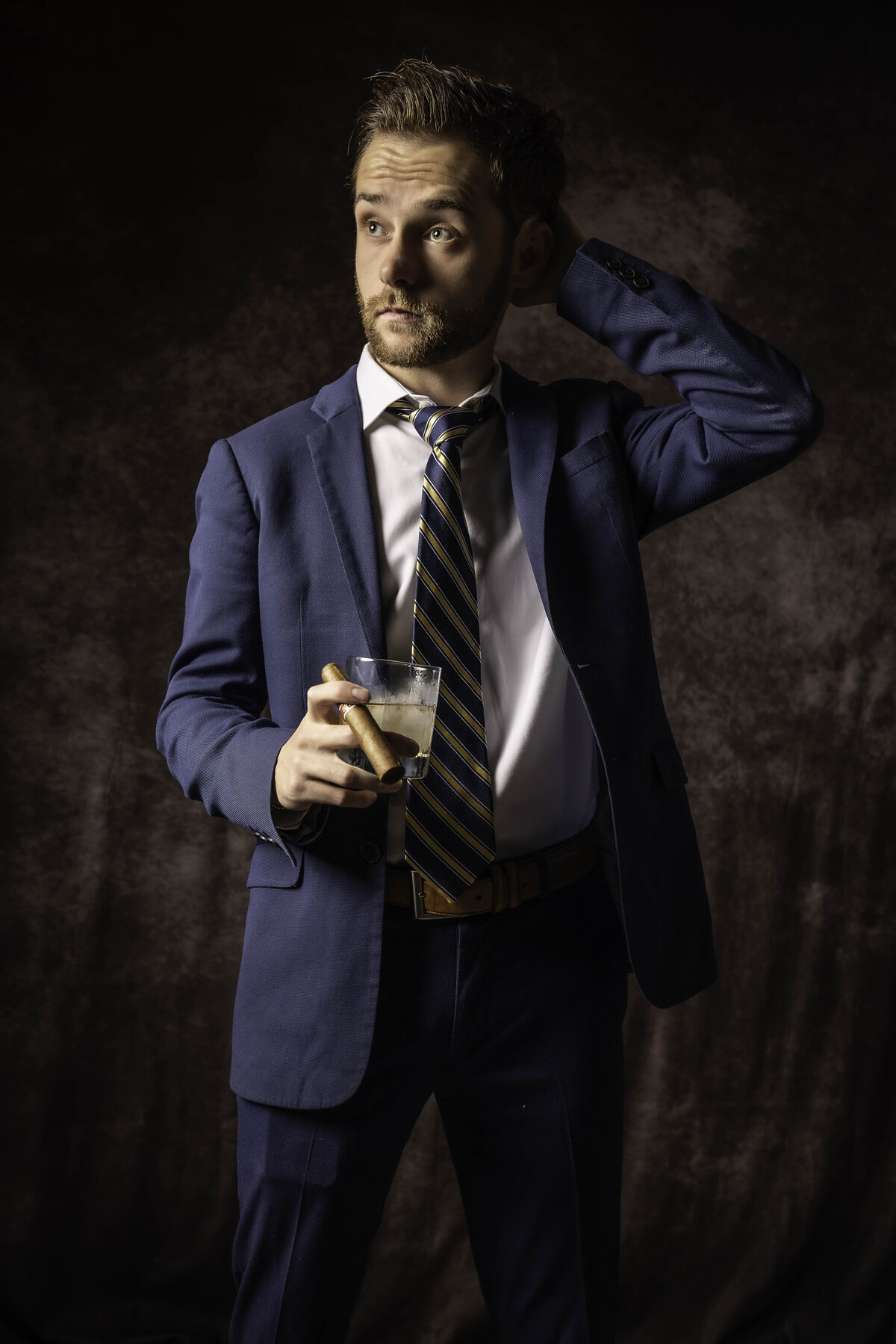 Professional headshot in CT of man in navy suit adjusting tie, posed against dark backdrop by Rob Faber Photography.