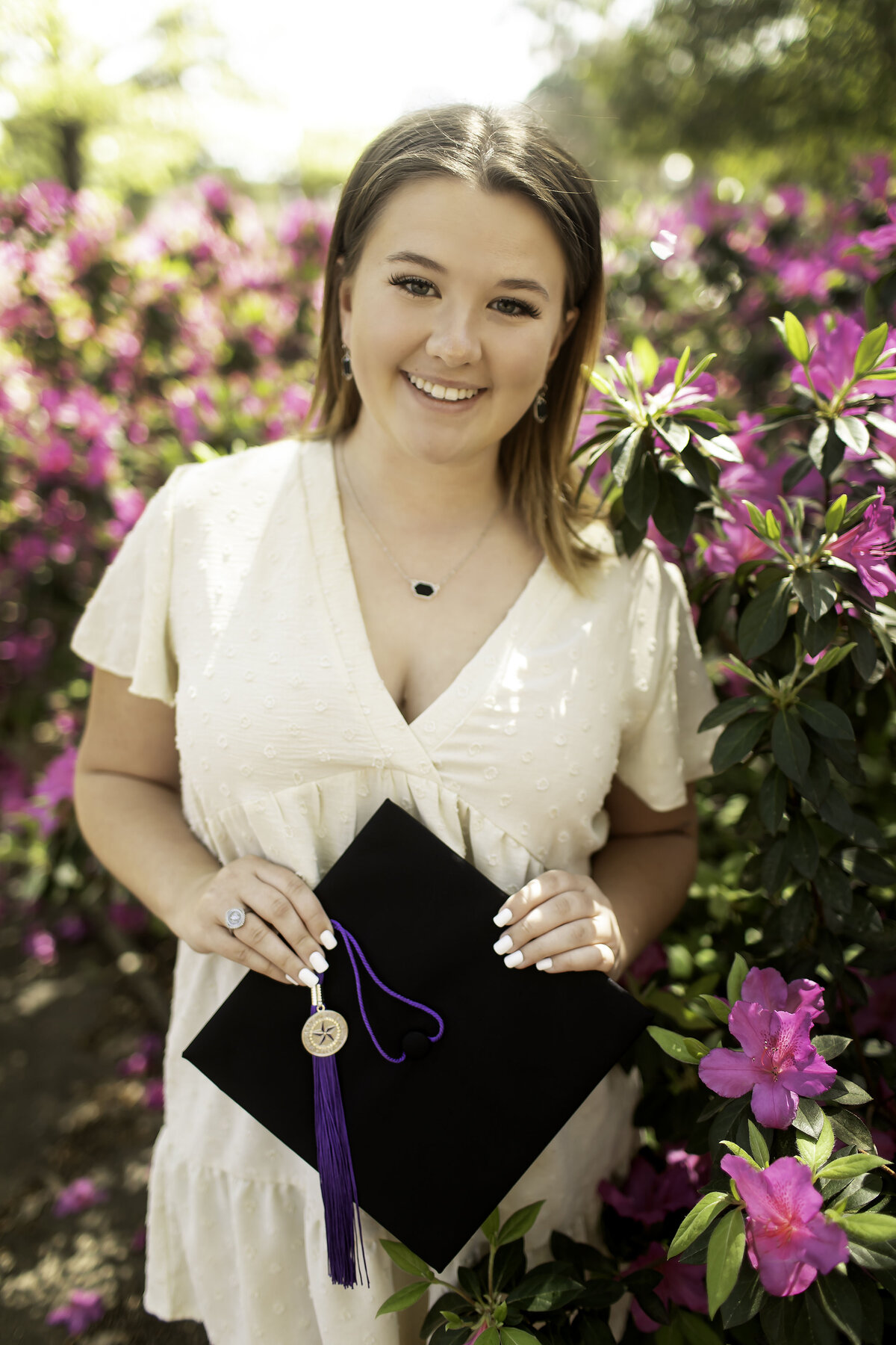 A senior holds their graduation cap in one hand, smiling at the camera